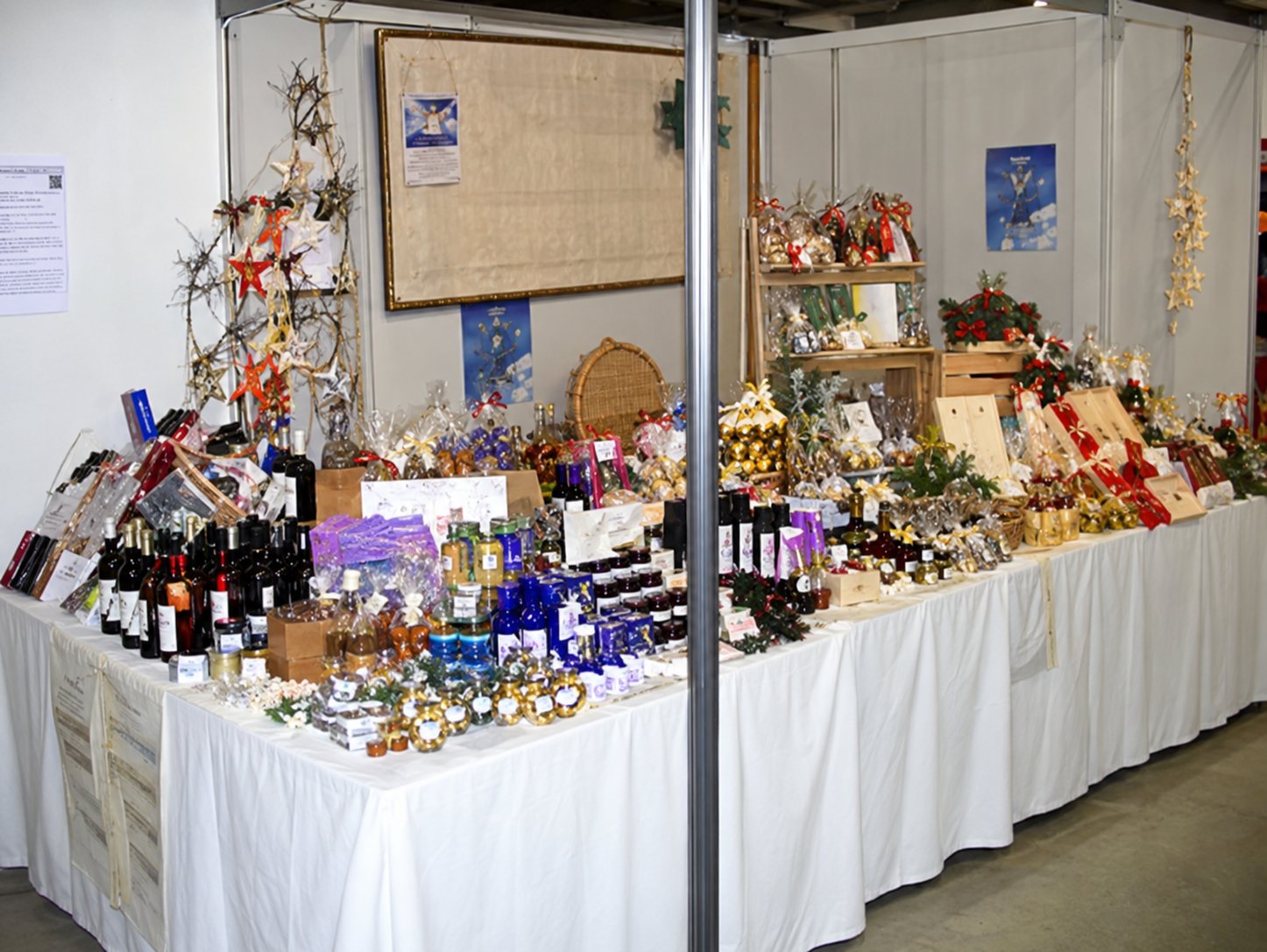 Un stand d'exposition avec une table recouverte d'une nappe blanche sur laquelle sont présentés de nombreux produits artisanaux, devant des panneaux muraux.